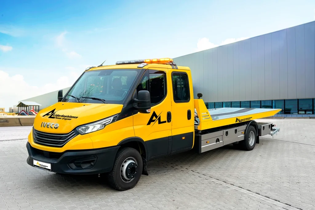 Żółta autolaweta marki Iveco LiderAssistance zaparkowana na utwardzonym placu. Pojazd wyposażony w nowoczesne oświetlenie ostrzegawcze oraz platformę do transportu pojazdów.